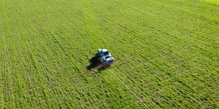 鸟瞰图蓝色老式拖拉机与肥料喷雾器处理小麦或大麦田与液体化学品