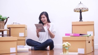 亚洲妇女搬到新房子使用电脑平板电脑购物的网上装饰。住房贷款和抵押概念视频素材模板下载