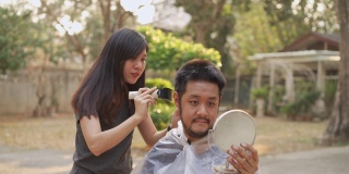 新冠肺炎疫情下，一名亚洲男子指着自己的头，要求在家里用剪子剪头发，以帮助拉平曲线