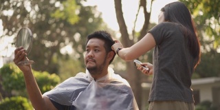 新冠肺炎疫情下，一名亚洲男子在家中拿着镜子为自己的夫妇理发