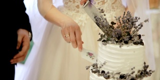 新娘和新郎切结婚蛋糕。新婚夫妇手中切下一块婚礼蛋糕。漂亮的婚礼蛋糕装饰着鲜花