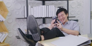 亚洲高级男子正坐在办公室里看着屏幕手机工作着，笑着开心的脸笑着开心的成功