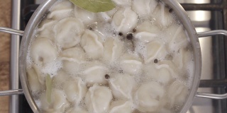 慢动作俯视图镜头香料与饺子在沸腾的水掉进锅里。自制饺子的制作过程。传统的俄罗斯食品。食品的背景。