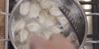 慢动作俯视图镜头煮饺子在沸腾的水在平底锅。男用手用漏勺在炖锅里搅拌饺子。传统的俄罗斯食品。食品的背景。