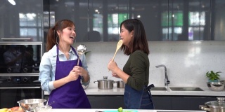朋友们喜欢在家里做饭。亚洲妇女在家庭厨房一起做饭。两个女人在厨房跳舞。