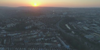 在英国南布里斯托尔郊区，宽阔的空中跟踪镜头经过一排排彩色的排屋，背景是落日
