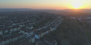 在英国布里斯托尔，空中飞过一排一排彩色梯田的郊区房屋，朝向夕阳