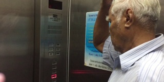 一个泰国裔老人在按电梯按钮