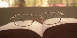 在一个温暖的阳光明媚的早晨，将一本打开的书和一副眼镜或眼镜放在木桌上，正面特写。孤立的背景。假日教育设计理念。