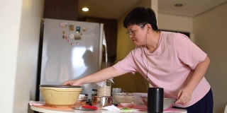 一位亚洲华人家庭妈妈在准备面团的同时，使用虚拟助手智能音箱来制作食谱和指导