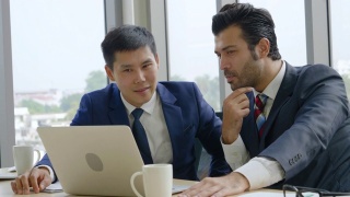 两名商人正坐在一个会议上，看着一台笔记本电脑讨论如何在公司现代化的办公室里帮助规划商业成功视频素材模板下载