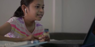 亚洲可爱的女孩学生戴着耳机，并与老师在电脑上聊天在网上学习课程。新冠肺炎疫情期间，通过视频电话在家学习的女性青少年。
