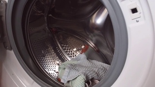 家庭主妇把衣服和毛巾放进洗衣机的滚筒里。客房管理和家居改善的概念视频素材模板下载