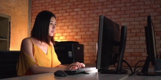 紧急，侧面的亚洲美丽的年轻女商人穿着不寻常的衣服有一个聚会，但工作到深夜电脑在现代办公室。积极的工作幸福感的概念。