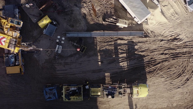 在一个阳光明媚的日子里，一架无人机在山谷里的一个石油和天然气钻井平台上直接拍摄了起重机拆卸钻机的画面