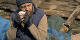一个无家可归的人在废墟附近喝热茶，在疫情期间帮助贫困和饥饿的人们