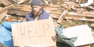 一名无家可归的男子在废墟附近用一个指示牌帮助，帮助在疫情期间贫穷和饥饿的人们