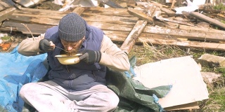 一个无家可归的人在废墟附近吃着盘子里的汤，在疫情期间帮助贫穷和饥饿的人们