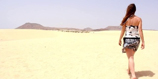一个孤独的女人在阳光明媚的日子里赤脚走在明亮的黄色沙丘上