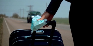 近距离观察戴医用口罩的年轻女性，以保护自己免受冠状病毒感染，她在路上带着带轮子的行李箱行走