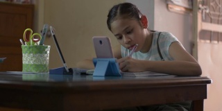 亚洲可爱的女孩使用手机和数字平板电脑在做作业期间在线上课。女青少年在家通过视频电话学习。