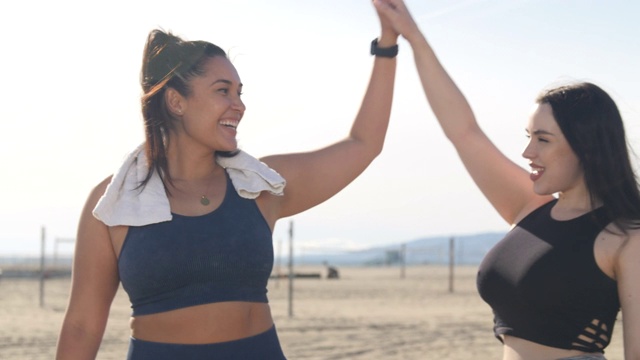 两个曲线优美的女人在海滩锻炼后击掌