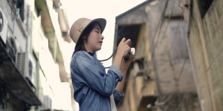 迷人的亚洲女性旅行者戴着复古软呢帽使用胶片相机拍照。享受暑假旅行。单独旅行的概念。