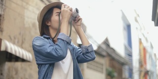 漂亮的潮女人戴着复古软呢帽，在泰国曼谷的一条小街上用胶卷相机拍照，享受东南亚的暑假旅游假期。