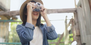 美丽的亚洲潮女人戴着复古软呢帽，在泰国曼谷的一条小街上用胶卷相机拍照，享受东南亚暑假旅游假期。