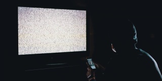胡德蒙面人的剪影与智能手机和看电视干扰
