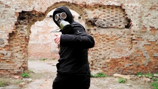 一个戴着防毒面具穿着黑色衣服的人跑在一座废弃的废墟上。跟踪者概念，核化学战争幸存者。缓慢的运动。视频素材模板下载