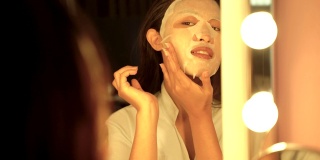 一名年轻的亚洲女子在浴室里敷面膜，看着自己的倒影