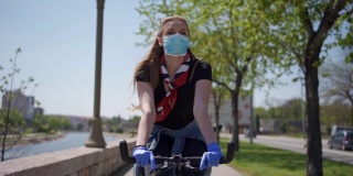 年轻女孩独自骑着自行车在城市海滨，在大流行期间应用所有的保护措施和社会距离
