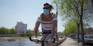 年轻人骑自行车独自在城市海滨，应用所有的保护措施和社会距离在大流行期间