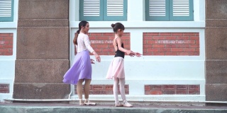 侧面图:泰国曼谷，一个阳光明媚的日子里，一名亚洲芭蕾舞少女在街上练习芭蕾舞，动作和当芭蕾舞老师的年轻女子一样。概念活泼的年轻妇女和孩子在周末的活动。