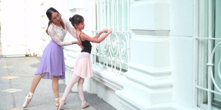 在泰国一个阳光明媚的日子里，在曼谷当地的街道上，一名亚洲青少年芭蕾舞演员在担任芭蕾舞老师时，按照年轻女芭蕾舞师的建议练习芭蕾舞。概念活泼的年轻妇女和孩子在周末的活动。