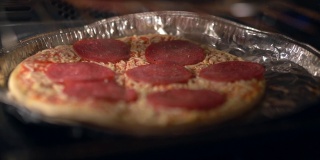 在家里用电炉自制意大利圆形披萨，美味的披萨香辣的东西。厨师用辣意大利腊肠、磨碎的马苏里拉奶酪和帕尔马干酪制作披萨。美味的披萨在烤箱中烹饪
