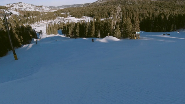 慢动作，无人机拍摄的滑雪者在完整的冬季装备完成一个跳跃与森林和滑雪升降机在背景在埃尔多拉滑雪度假村附近博尔德，科罗拉多州在一个明亮，阳光明媚的日子
