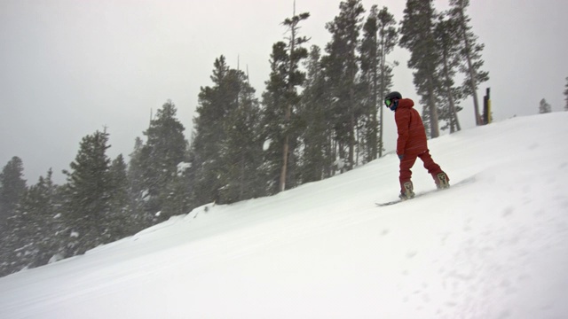 慢动作拍摄的一个滑雪板穿着完整的冬季装备单板滑雪在埃尔多拉滑雪度假村附近的博尔德，科罗拉多州被滑雪电梯和森林在一个下雪，阴天