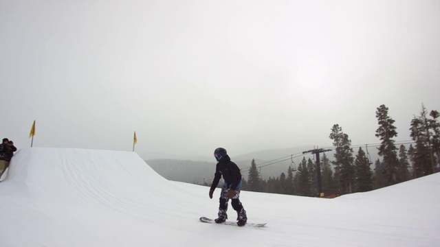 一个滑雪板穿着完整的冬季装备完成一个“出租车5火箭”在一个滑雪跑在埃尔多拉滑雪度假村附近博尔德，科罗拉多州在一个下雪的，阴天，而摄影师拍摄他/她的照片的魔术