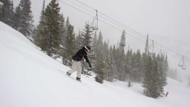 一个摄影师的慢动作拍摄的照片在完整的冬季装备滑雪板完成一个“西瓜抓取”的技巧在一个跳跃与森林和滑雪缆车在背景在博尔德附近的埃尔多拉滑雪度假村，科罗拉多州在一个下雪的，阴天