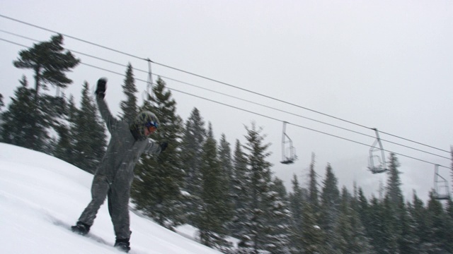 在科罗拉多州博尔德附近的埃尔多拉滑雪度假村，一名摄影师躺下并拍下了一名滑雪板在完整的冬季装备完成一个“后空翻Tucknee”跳跃技巧与森林和滑雪缆车为背景的慢动作镜头，