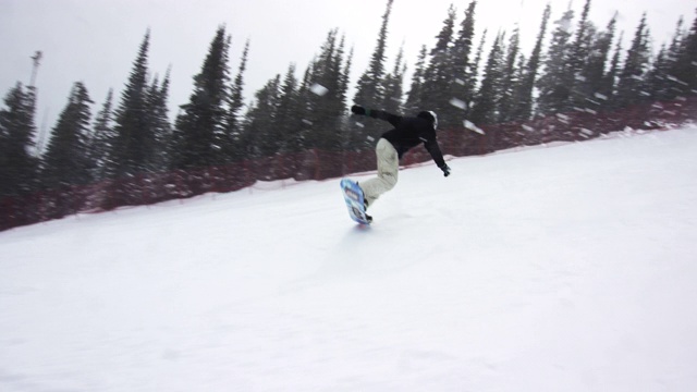 慢动作拍摄的滑雪板穿着完整的冬季装备滑雪板下的滑雪跑道周围的埃尔朵拉滑雪度假村附近的博尔德，科罗拉多州在一个下雪，阴天，雪花遍布