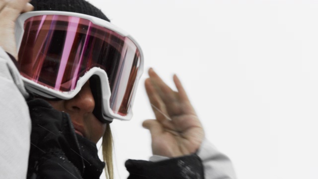一个微笑的十几岁女子滑雪板戴上她的护目镜准备在一个多云的冬日滑雪板
