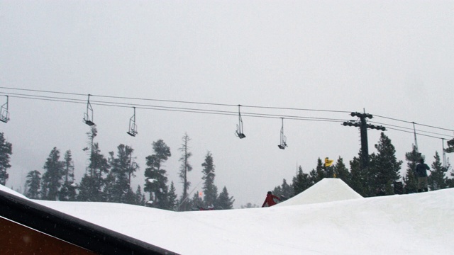 完成一个“驾驶室900开关尾巴”技巧与森林和滑雪缆车在背景在科罗拉多州博尔德附近的埃尔多拉滑雪度假村在一个下雪的，阴天从远处