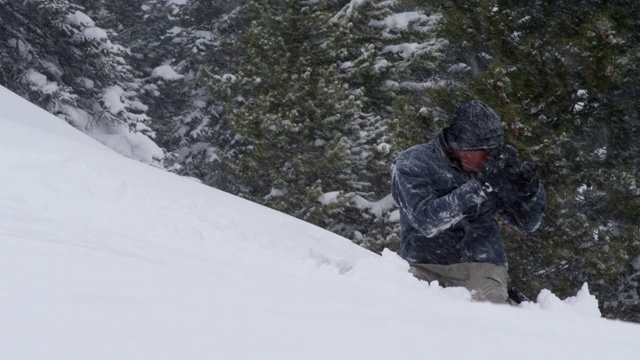 一个摄影师在完整的冬季装备拍摄的照片滑雪板完成在博尔德附近的埃尔多拉滑雪度假村跳跃的技巧，科罗拉多州在一个下雪的，阴天