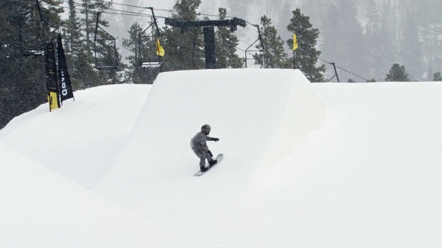 完成一个“前侧360 Tucknee”技巧与森林和滑雪缆车在背景在科罗拉多州博尔德附近的埃尔多拉滑雪度假村在一个下雪的，阴天从远处