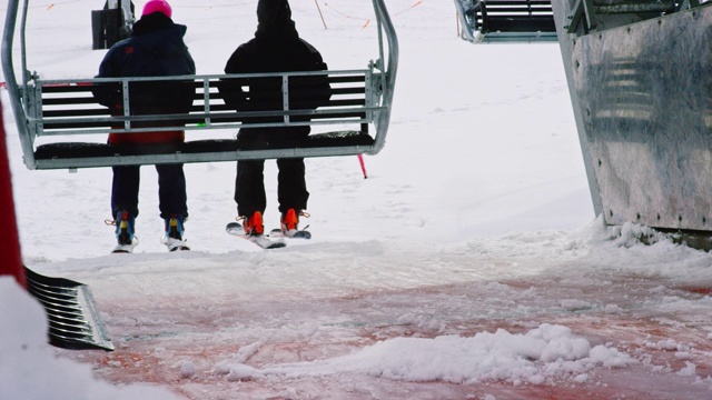 一个滑雪缆车举起两个滑雪者，而有人铲雪从滑板平台在一个滑雪场在冬天