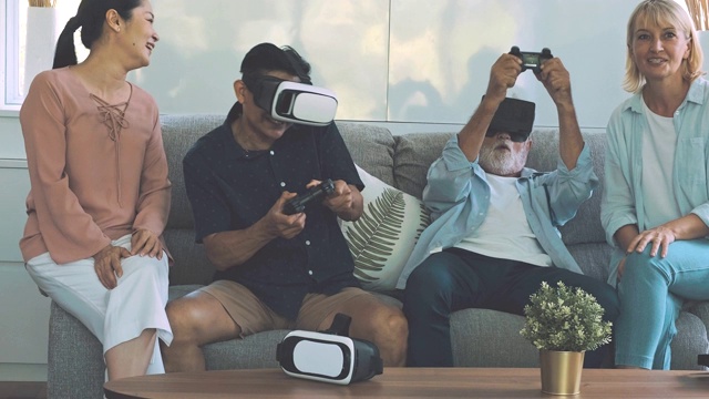 一群老年人在客厅玩VR游戏。白人，亚洲人，泰国人坐在家里的沙发上。退休生活方式的概念。