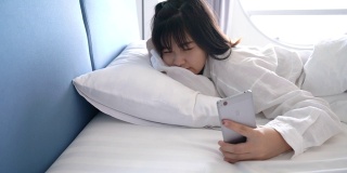 亚洲女人醒来和睡眠与智能手机闹钟，她在酒店房间小睡早上旅游游客概念4k分辨率